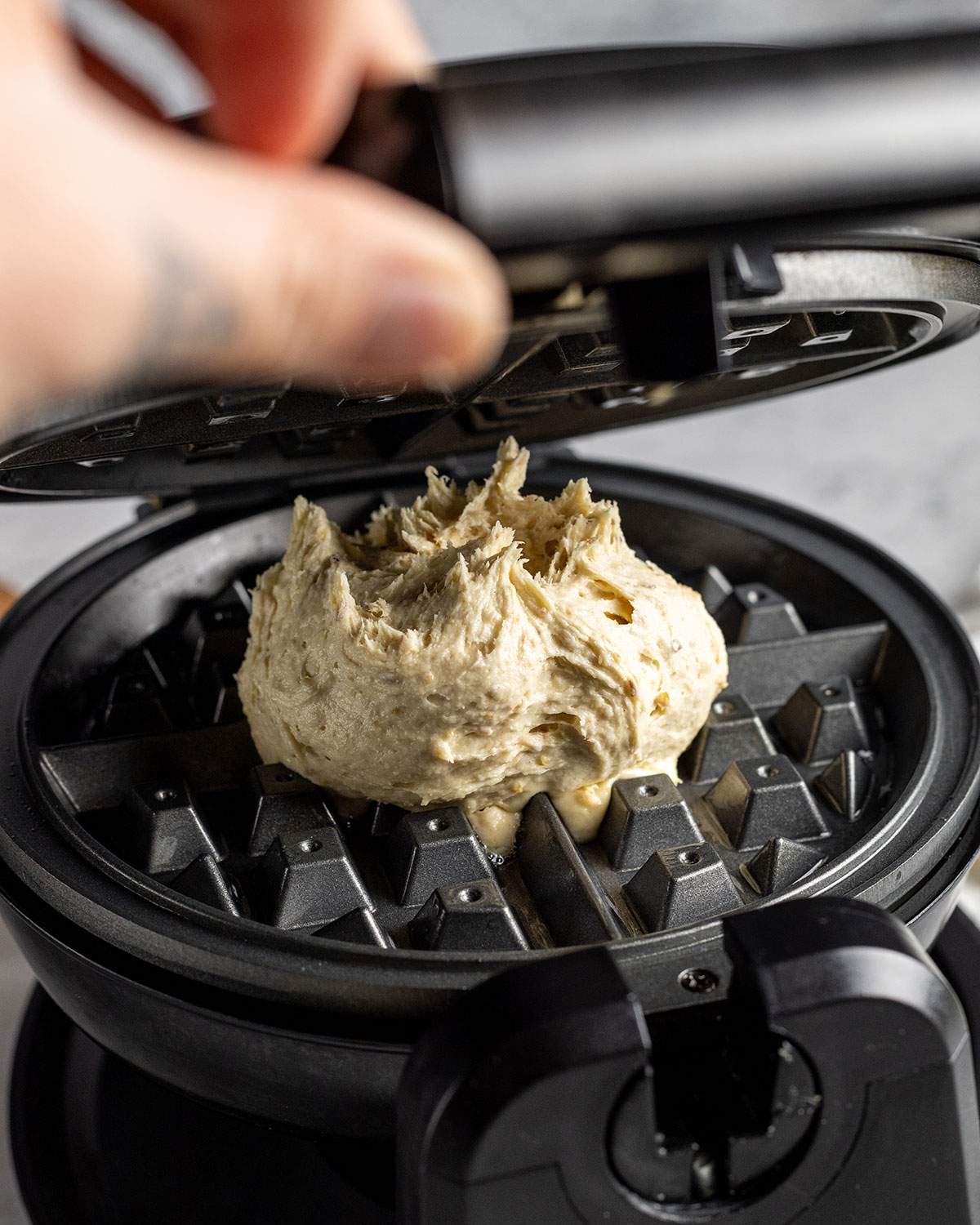 a hand closing a waffle maker onto vegan waffle batter