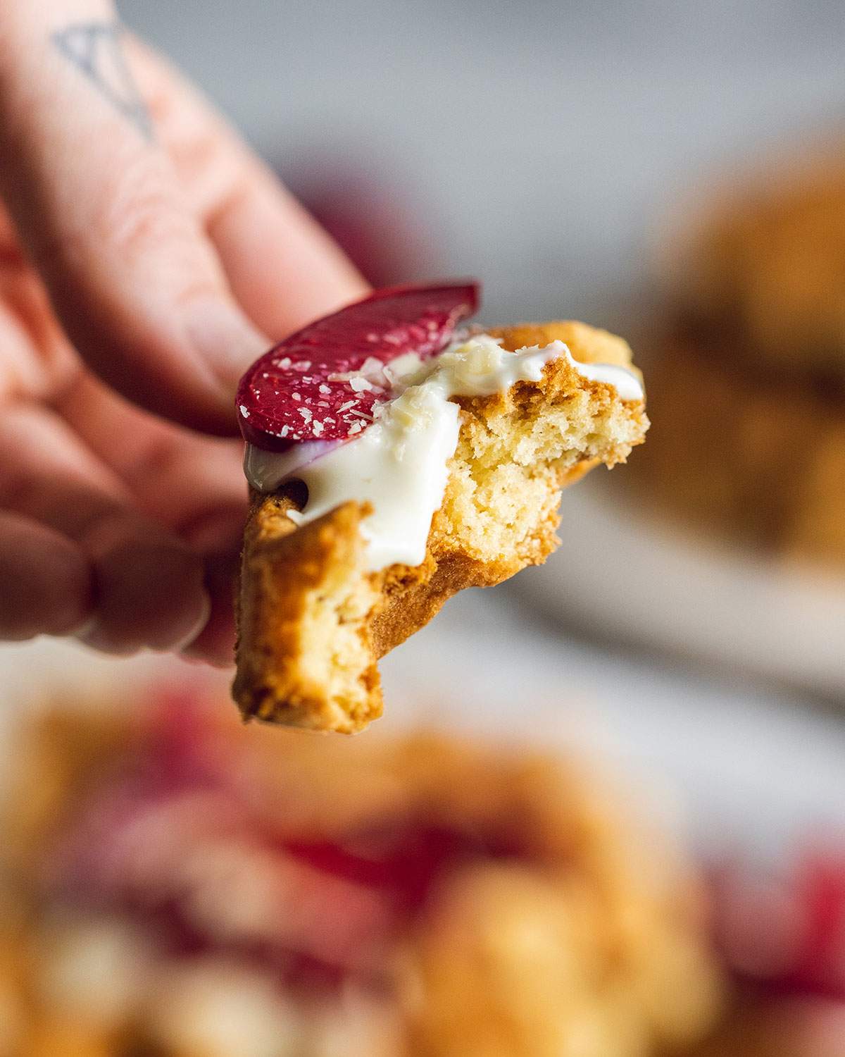 a hand holding a piece of condensed milk waffle with vegan yogurt and caramelized plums on top