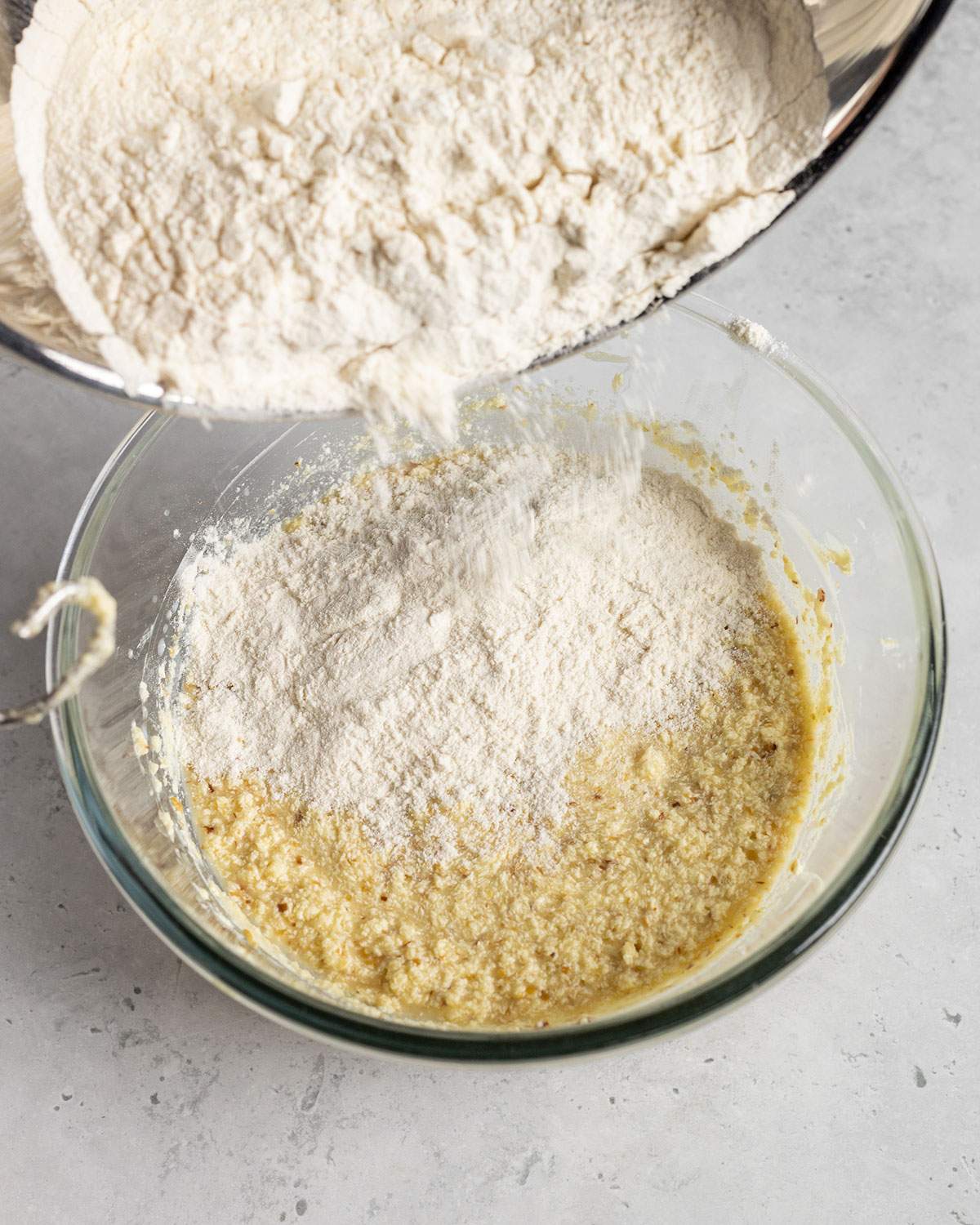 adding dry ingredients into a wet batter in a glass bowl