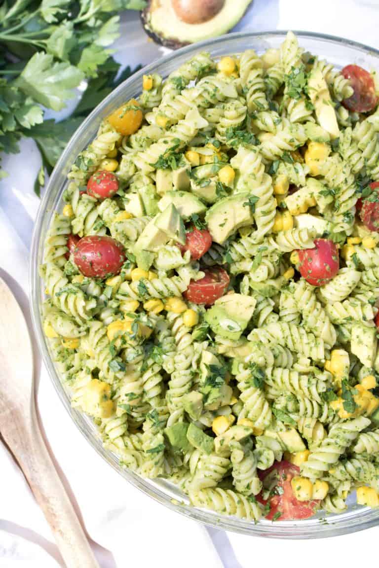 a serving bowl filled with green vegan avocado pasta salad with cherry tomatoes