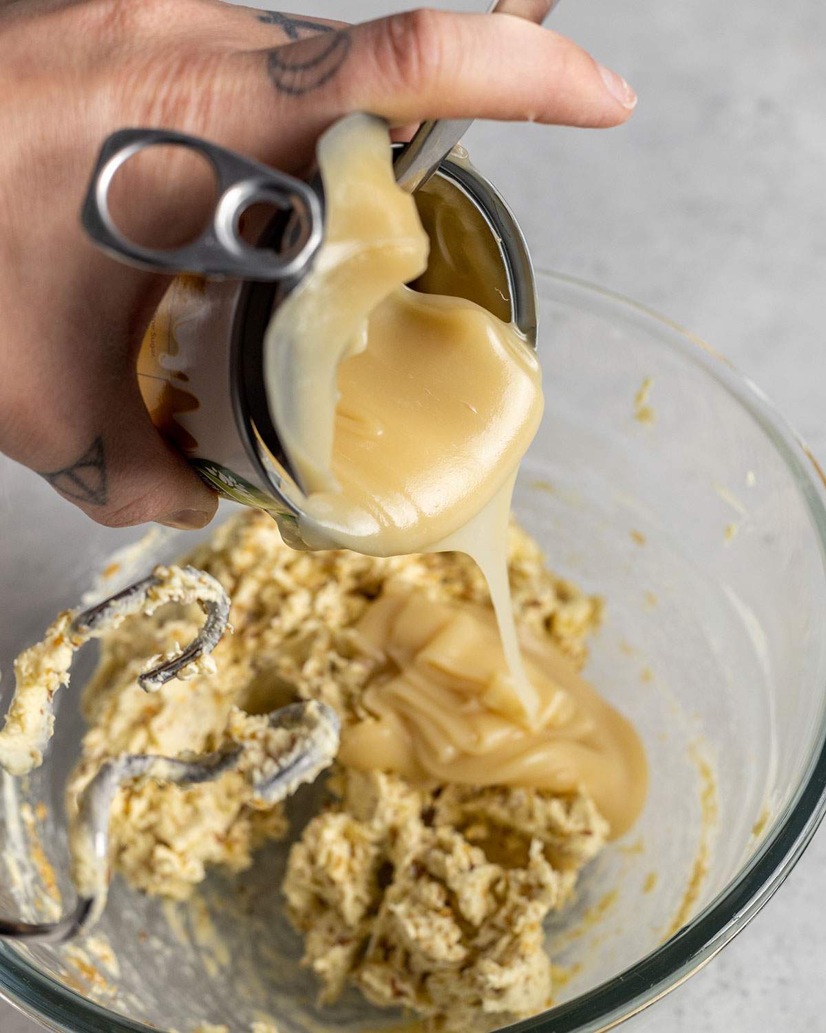 pouring condensed milk into batter in a mixing bowl