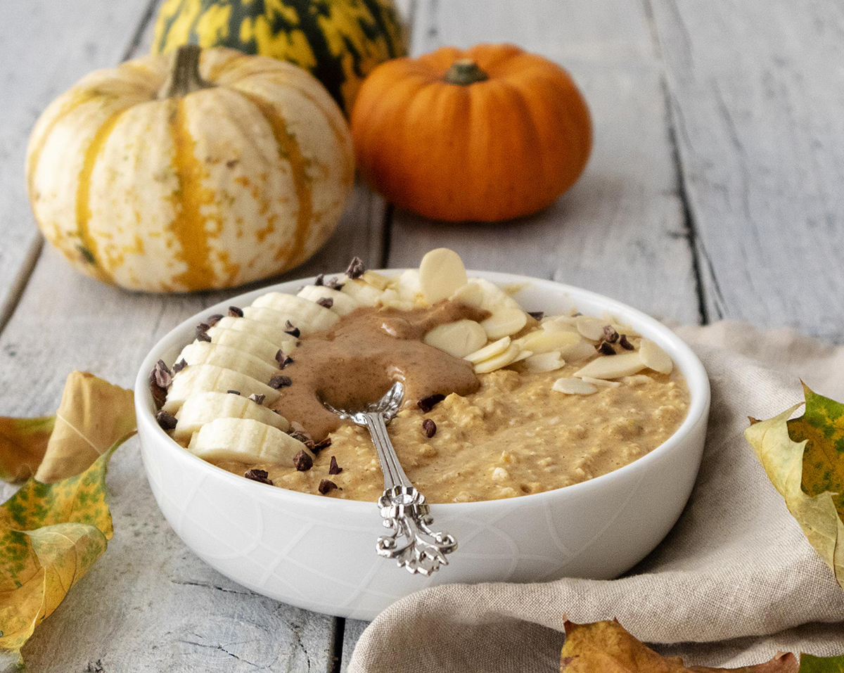 a bowl of pumpkin spice porridge on a white wooden table with pumpkins in the background