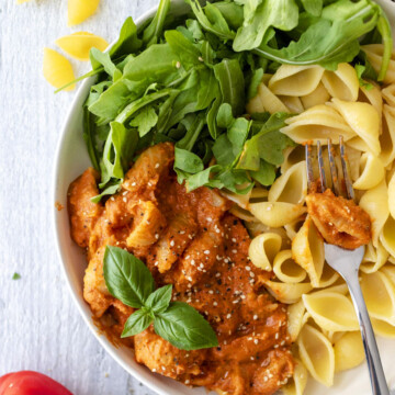 vegan roasted red pepper pasta sauce with pasta and arugula in a white bowl