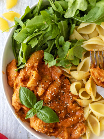 vegan roasted red pepper pasta sauce with pasta and arugula in a white bowl