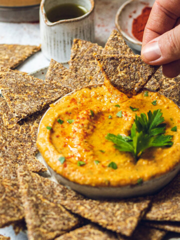 a spicy vegan butter bean dip in a bowl and an apple cracker being dipped into it