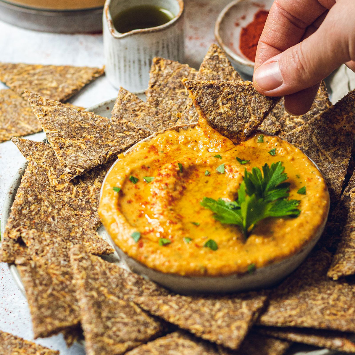 a spicy vegan butter bean dip in a bowl and an apple cracker being dipped into it