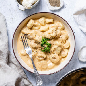 a white bowl filled with vegan tortellini and a creamy cauliflower alfredo sauce with pepper and fresh herbs on top