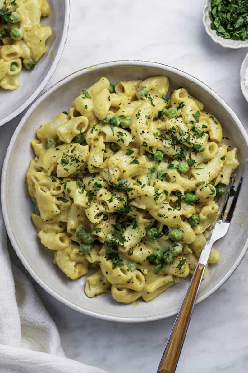 a plate with vegan mac and cheese, fresh herbs sprinkled on top and a fork on the side