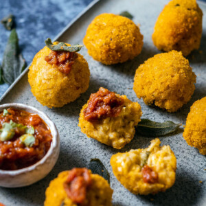 vegan arancini balls on a serving platter alongside crispy sage leaves and tomato sauce