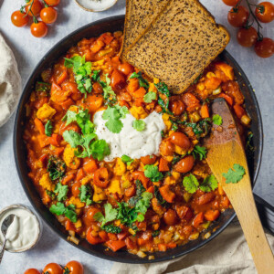 vegan shakshuka in a large skillet with toasted bread on the side, a dollop of coconut yogurt in the middle and fresh coriander on top