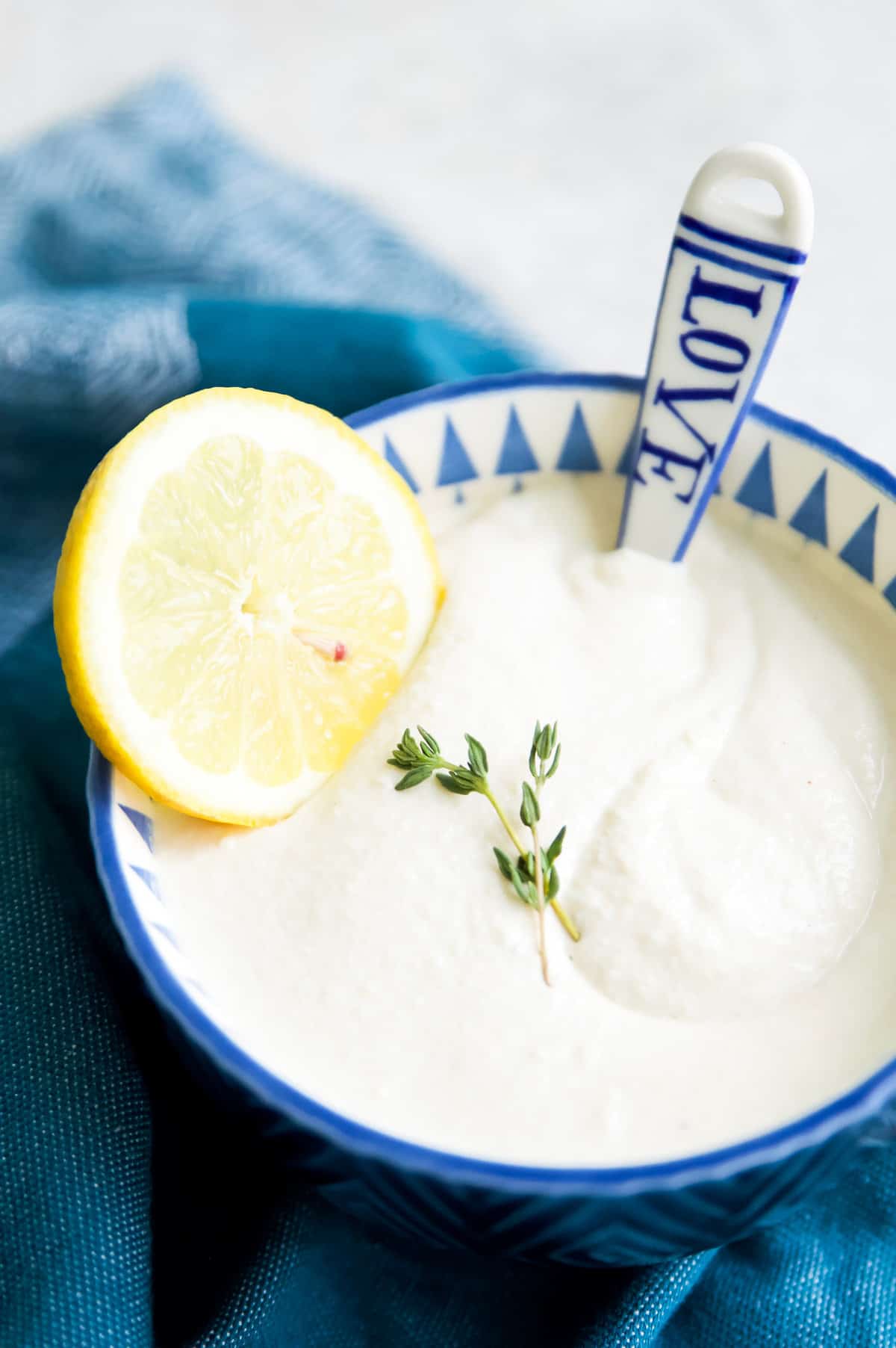 a small blue bowl filled with vegan sour cream, a spoon resting on the edge and a lemon slice on the side