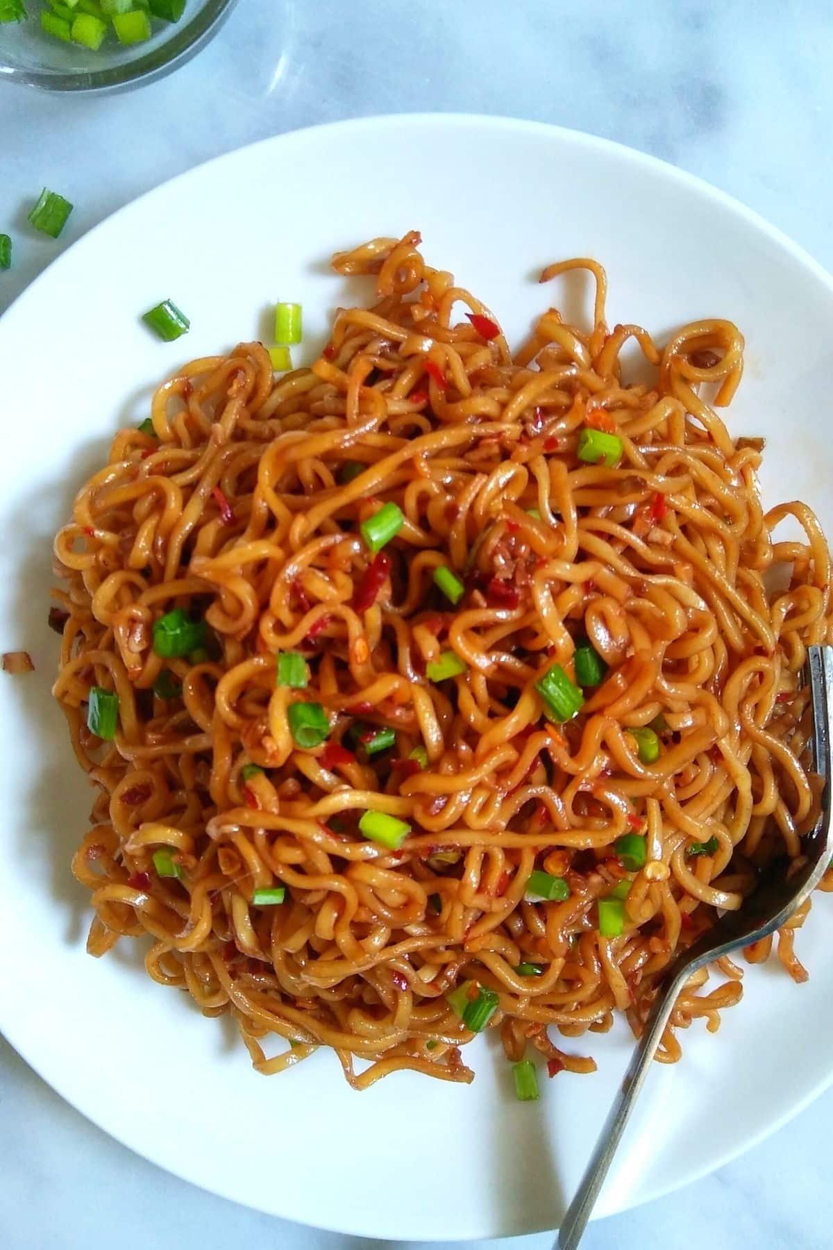 a white plate filled with spicy ramen noodles and green spring onions on top