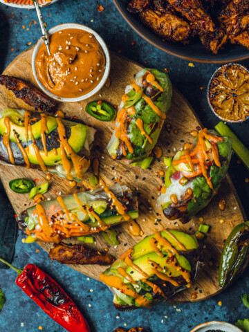 vegan summer rolls on a wooden chopping board with a peanut satay dip on the side