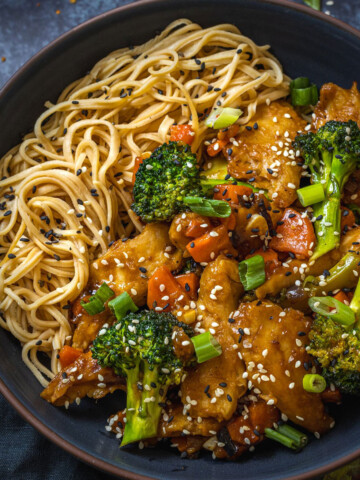 a black bowl filled with noodles and vegetables alongside homemade vegan teriyaki sauce