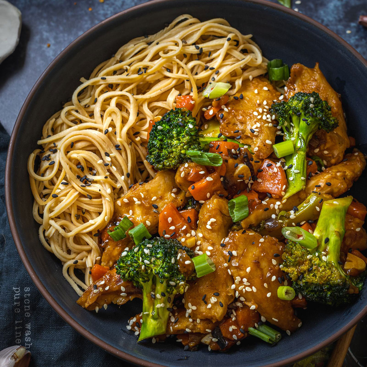 a black bowl filled with noodles and vegetables alongside homemade vegan teriyaki sauce