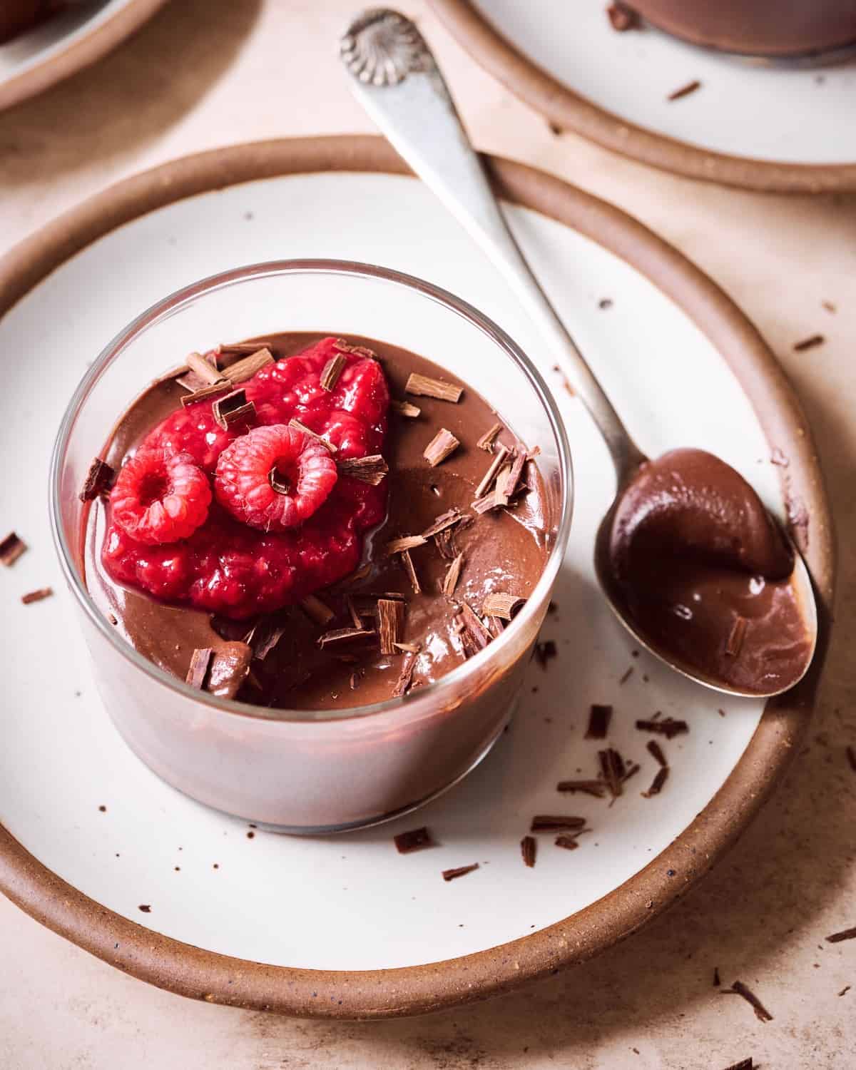 smooth tofu chocolate mousse with raspberries on top in a glass jar with a spoon on the side