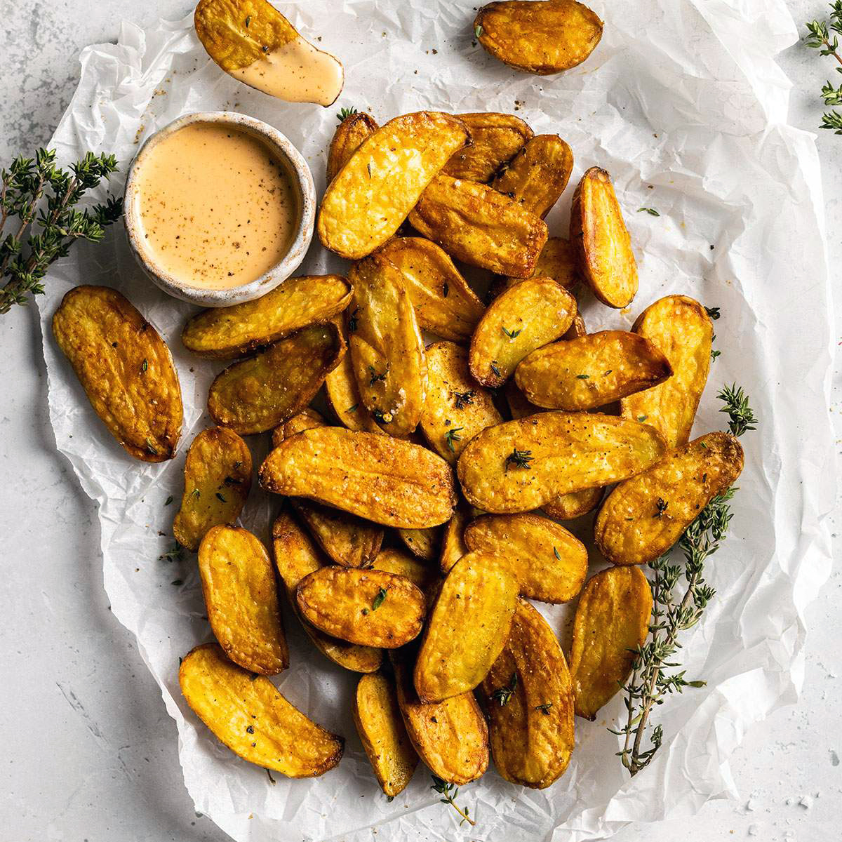 air fryer fingerling potatoes on a white parchment with a dip on the side and fresh thyme