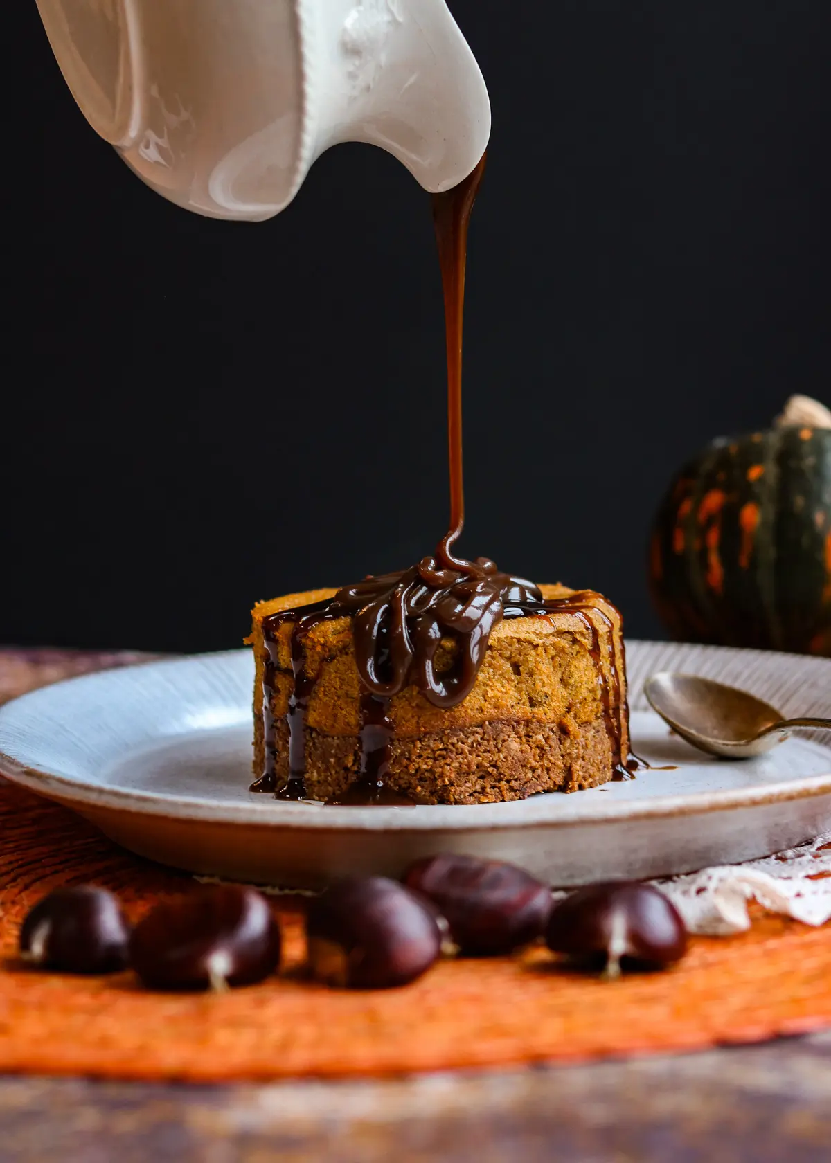 A set of small pumpkin cheesecakes with a crumbly graham cracker crust, topped with whipped cream and chopped nuts. The cheesecakes are made with a silken tofu filling, creating a creamy and protein-rich alternative to traditional cheesecake. They sit on a white plate, adding a contrast to the colorful and vibrant dessert.