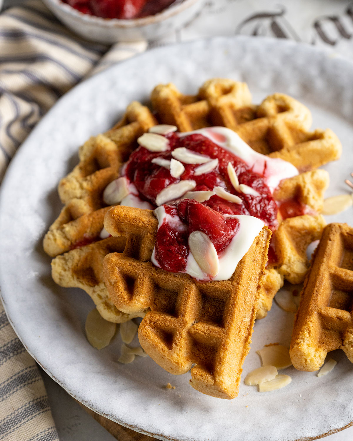 close up of vegan condensed milk waffles on a white plate with dairy free yogurt and strawberries on top