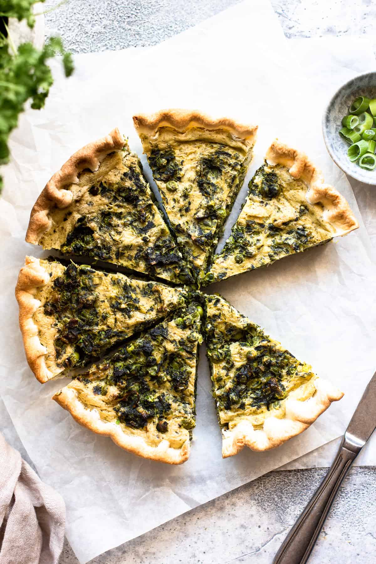 A slice of vegan spinach quiche on a plate, garnished with fresh herbs. The quiche is made with a creamy filling of silken tofu, spinach, and vegan ricotta cheese.