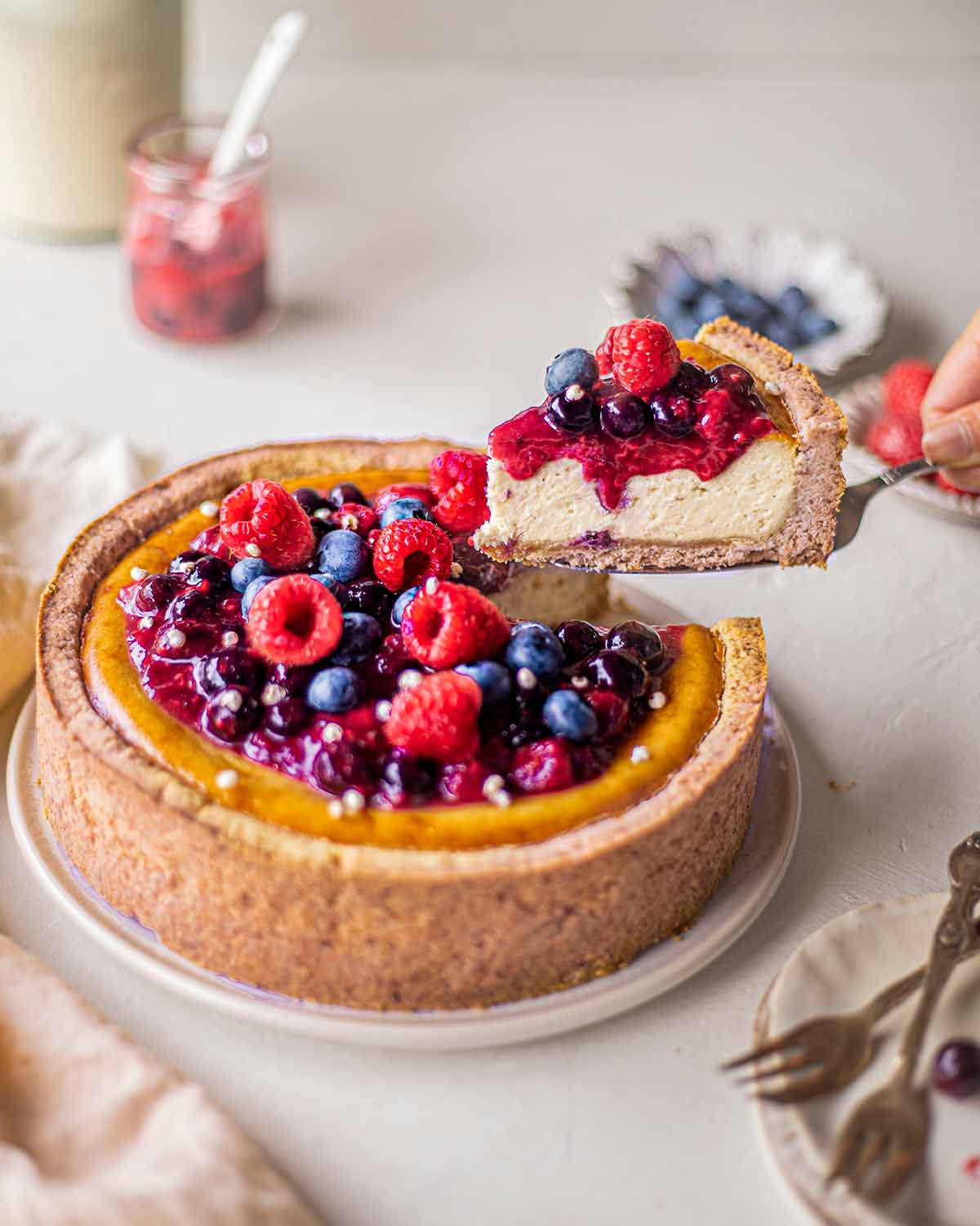 A slice of baked vegan cheesecake with a graham cracker crust and a creamy filling made from silken tofu. The cheesecake is topped with fresh berries and mint leaves, adding a pop of color and flavor to the dessert.