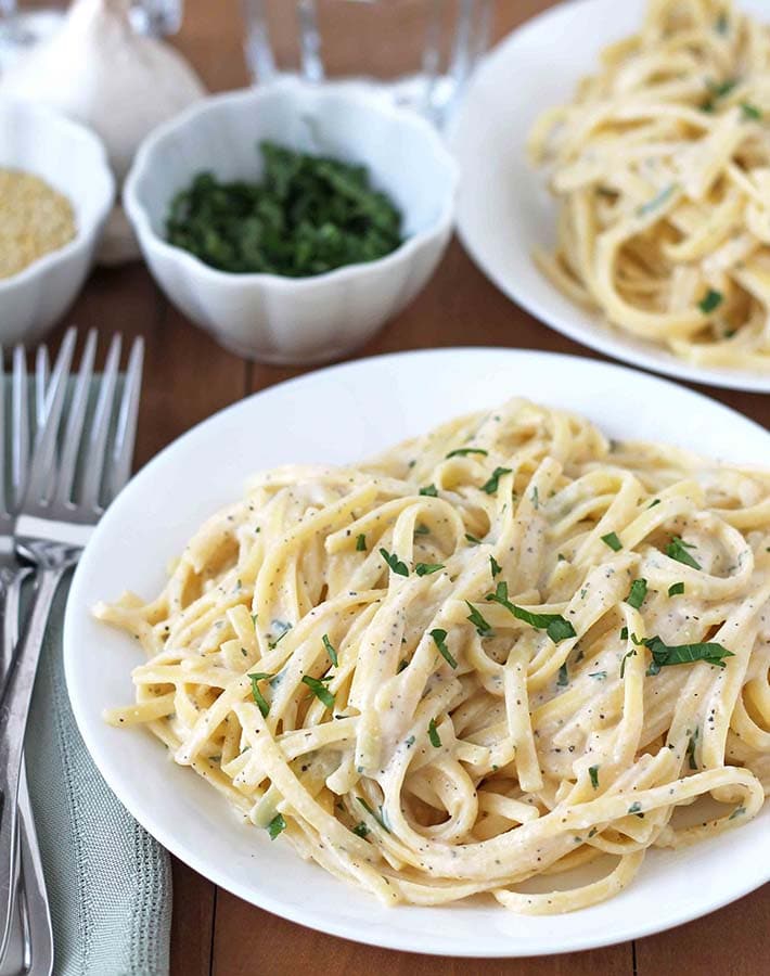 A plate of creamy vegan garlic pasta, topped with chopped parsley and red pepper flakes. The pasta is made with a silken tofu-based sauce, creating a protein-rich and flavorful alternative to traditional cream-based pasta sauces.