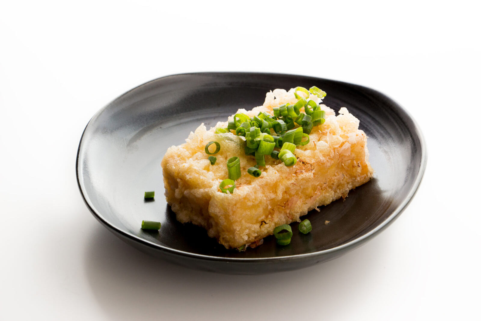 A plate of crispy fried Agedashi tofu, garnished with green onions and grated daikon, served with a side of dipping sauce.
