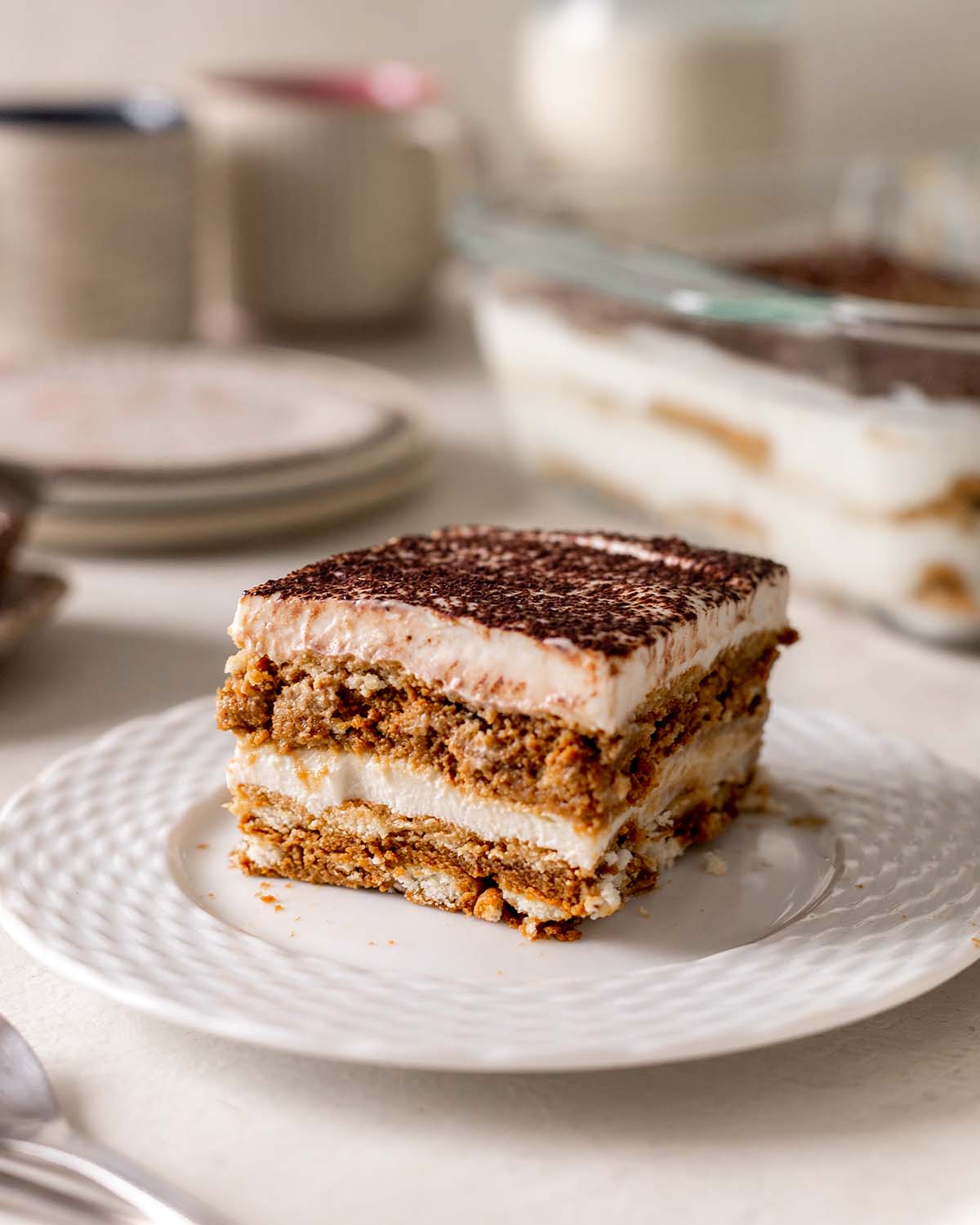 photo of vegan tiramisu on a white plate, topped with cocoa powder. The creamy filling is made with silken tofu and cocoa, creating a delicious and healthy dessert that's perfect for chocolate lovers.