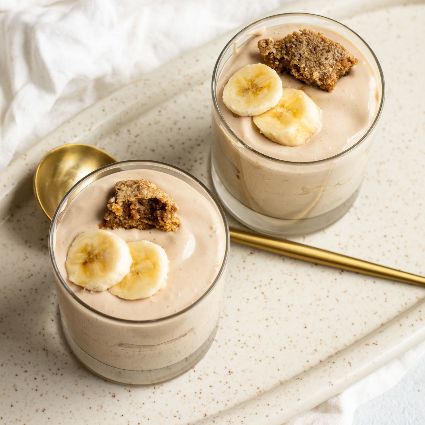 A bowl of banana vanilla silken tofu pudding with cookie crumble topping, garnished with fresh mint leaves and sliced banana.