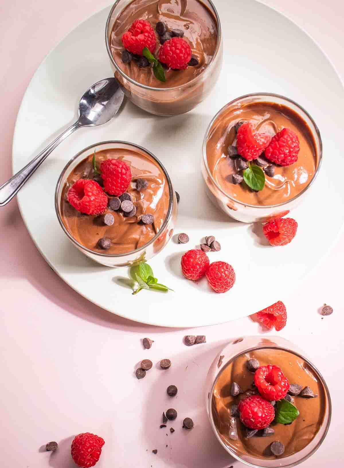 A close-up photo of a chocolate dessert in a white bowl garnished with fresh berries and mint leaves. The dessert is a chocolate mousse made with silken tofu, giving it a creamy and smooth texture.