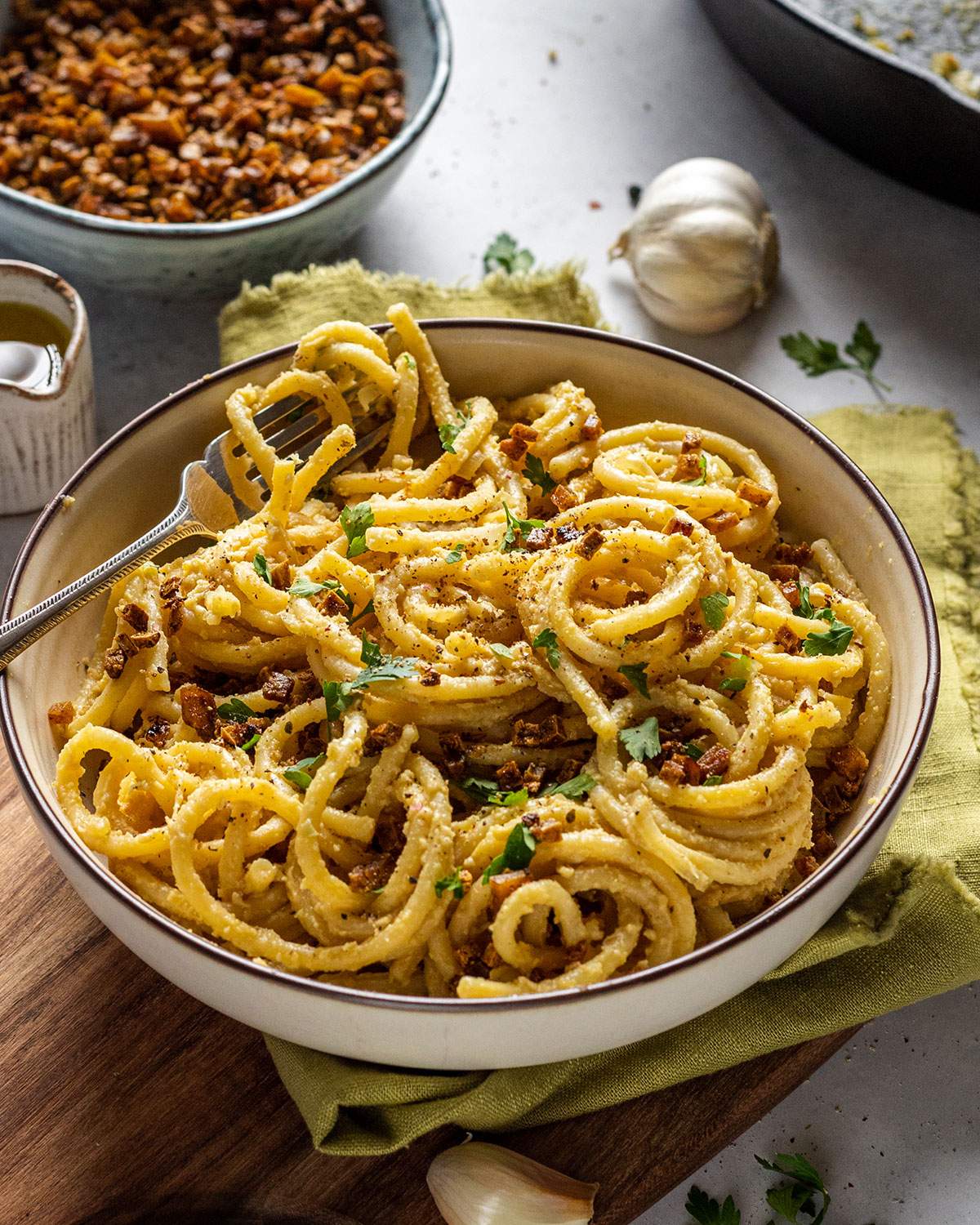 a white bowl filled with vegan spaghetti carbonara with smoked tofu bacon bits