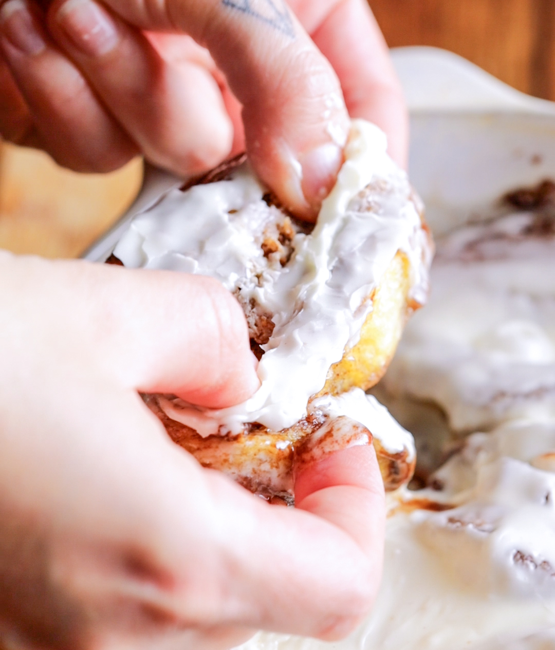 a hand lifting a cinnamon roll out of an oven dish