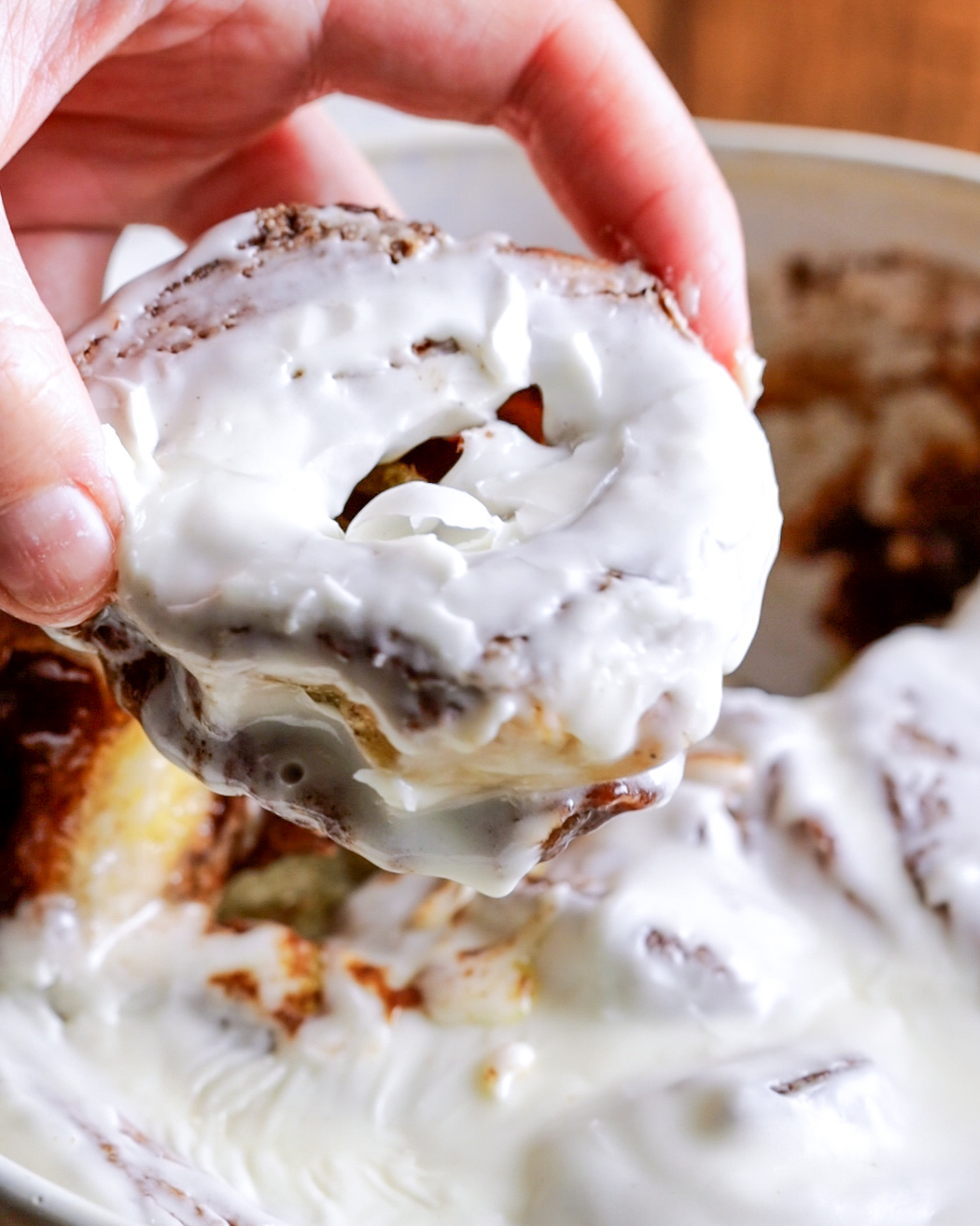 a hand lifting a cinnamon roll out of an oven dish