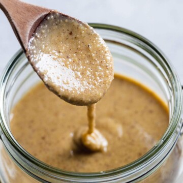 a wooden spoon lifting brazil nut butter out of a glass jar