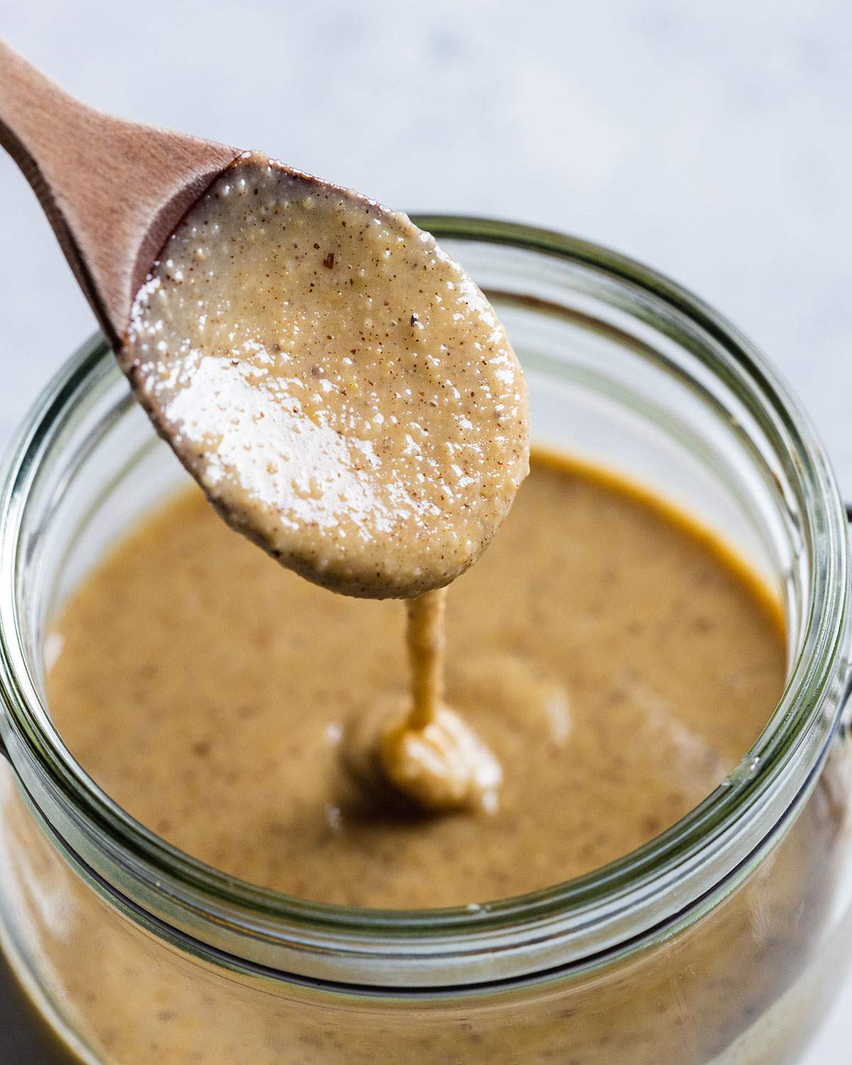 a wooden spoon lifting brazil nut butter out of a glass jar