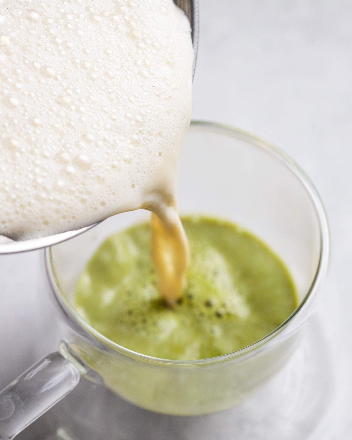 pouring frothed vanilla milk onto matcha tea