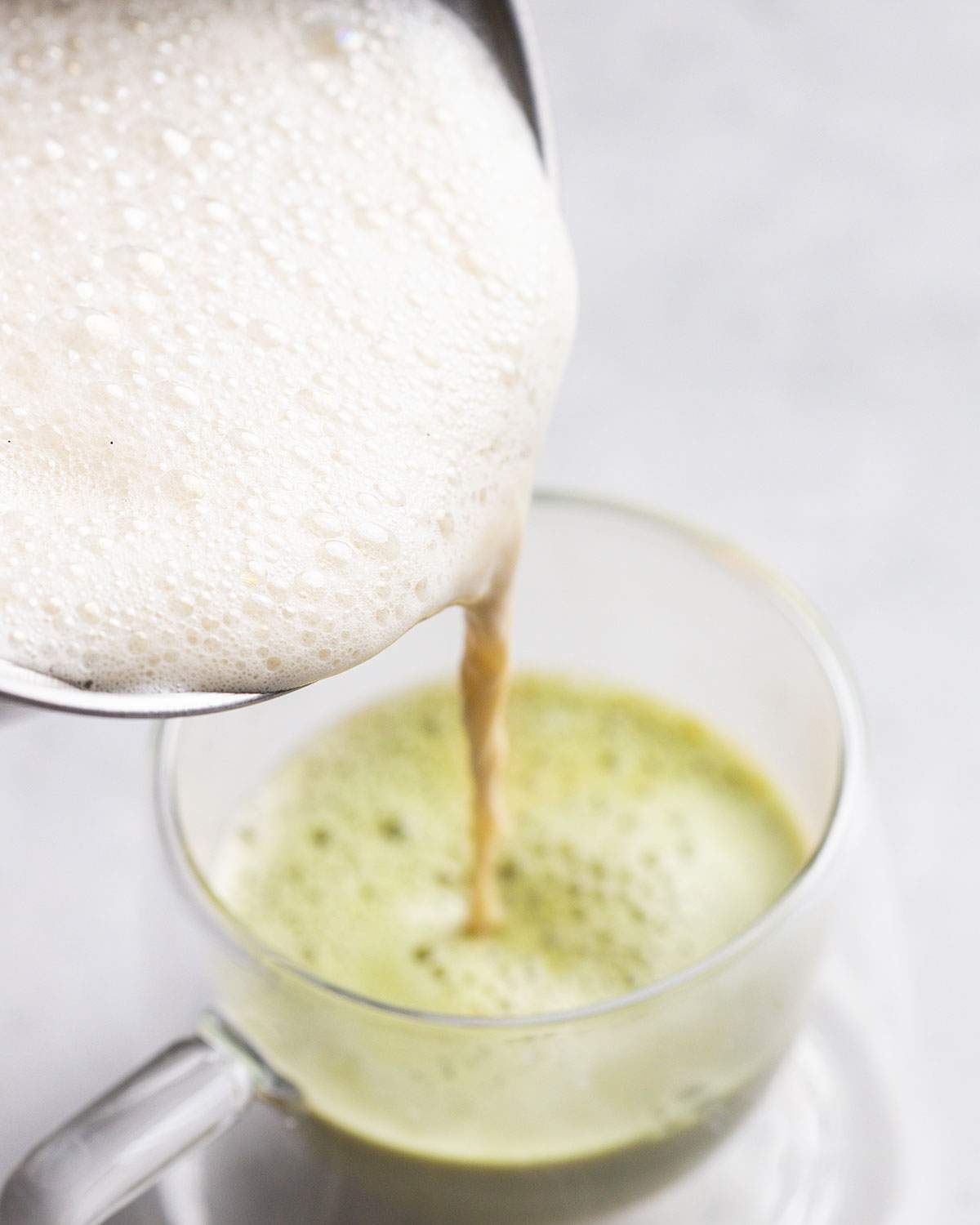 pouring frothed vanilla milk onto matcha tea