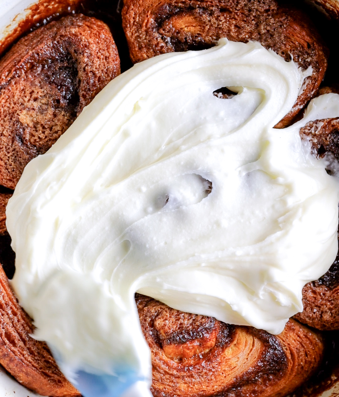 spreading frosting across baked cinnamon rolls