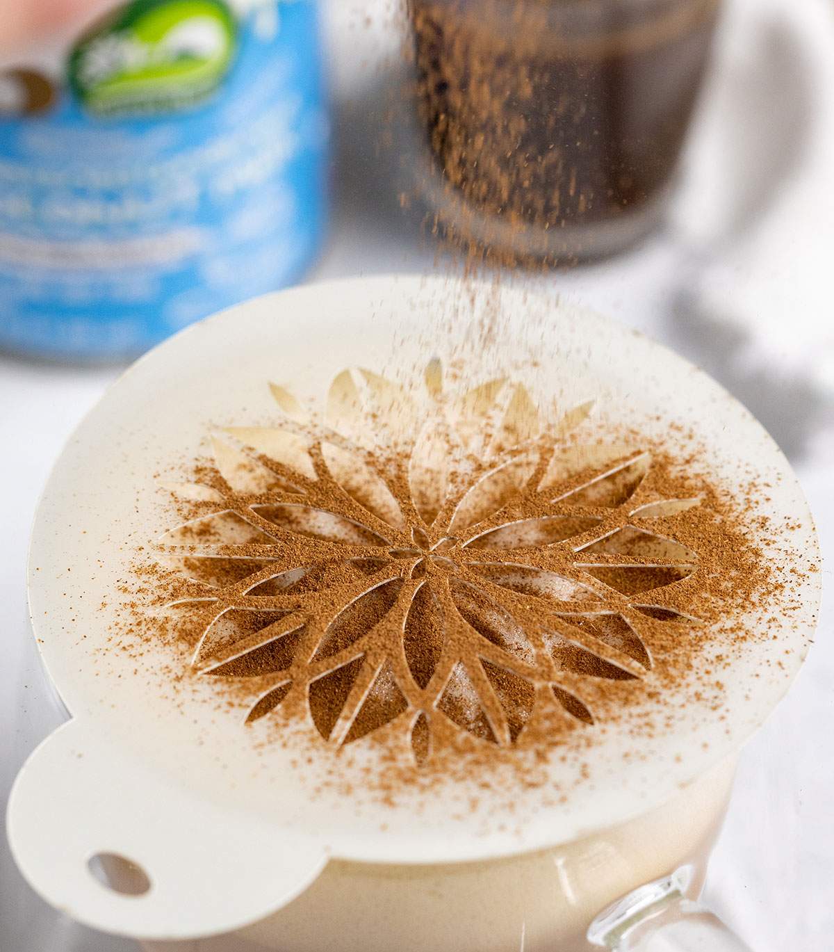 sprinkling cinnamon onto a coffee with a mandala stencil