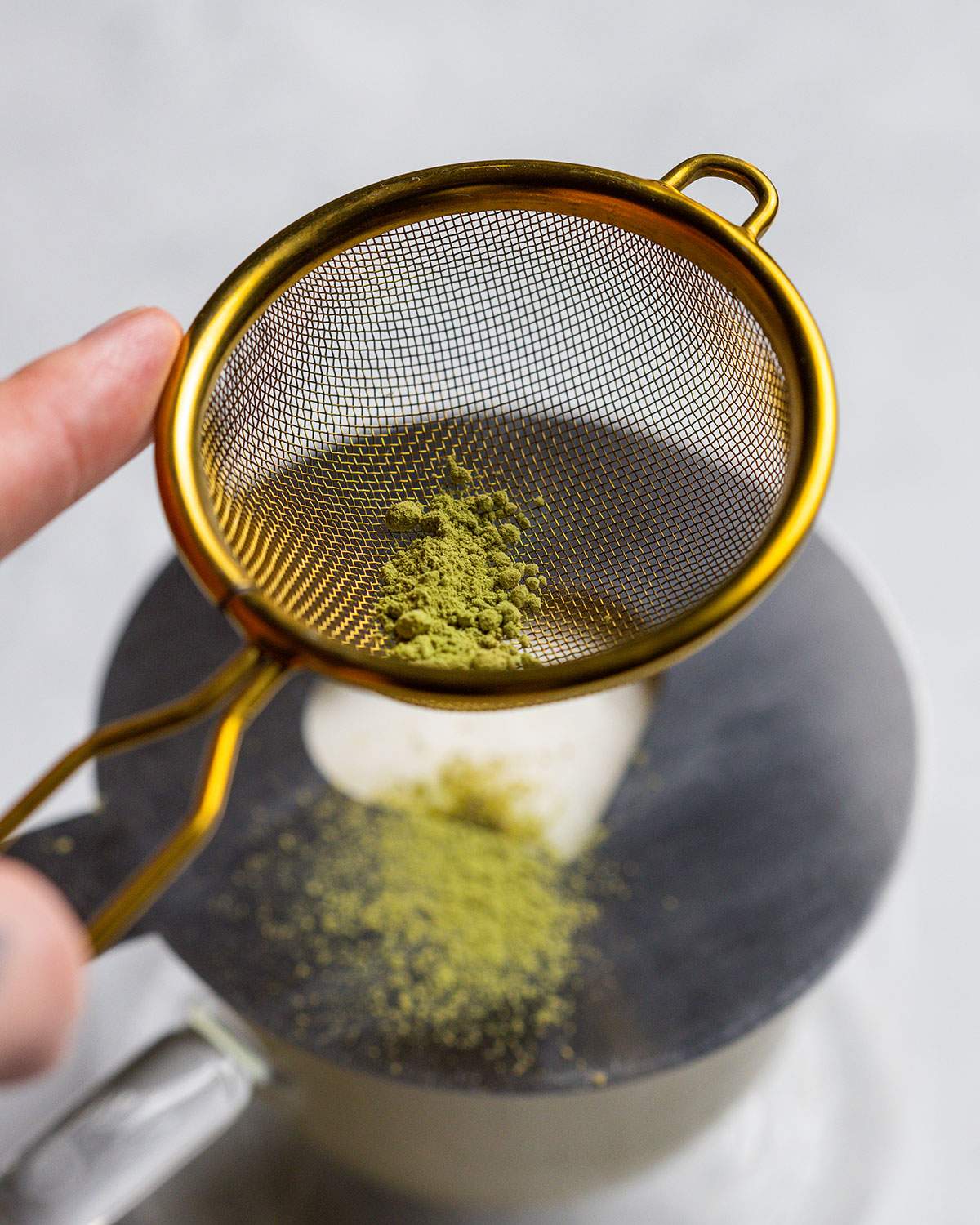 sprinkling matcha powder on top of a vanilla matcha latte