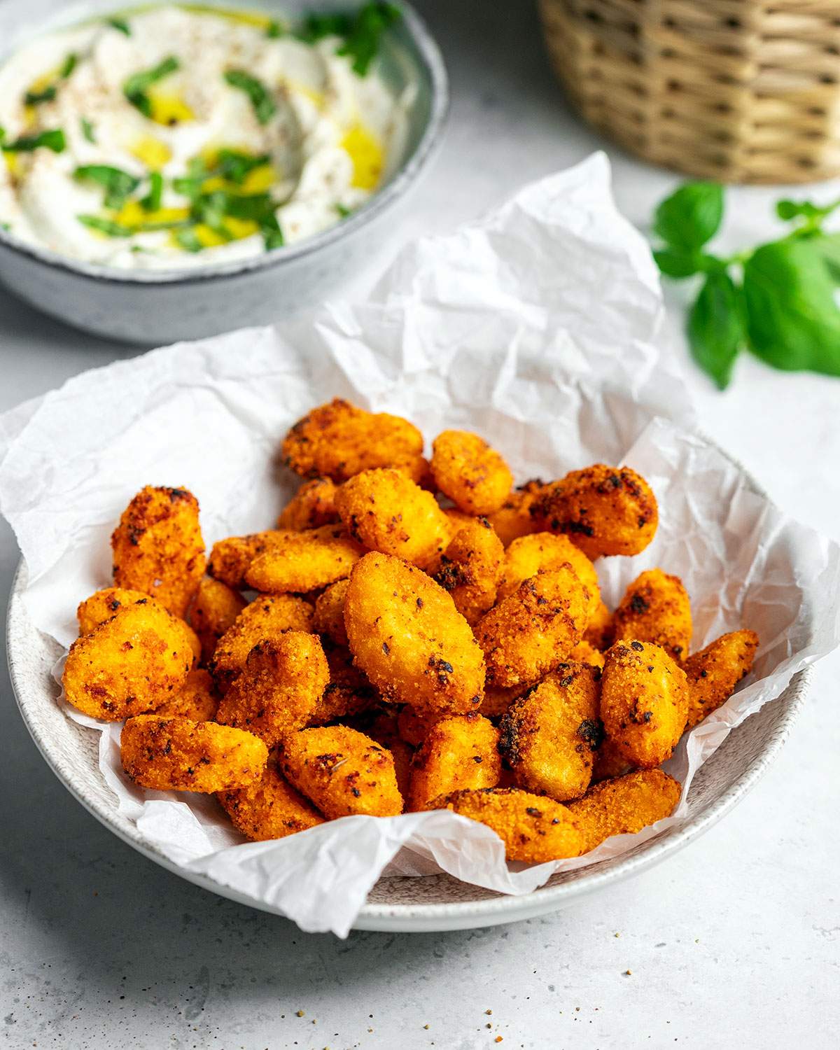 A bowl filled with air fryer gnocchi on a white table with a whipped cream cheese dip and fresh basil next to it.