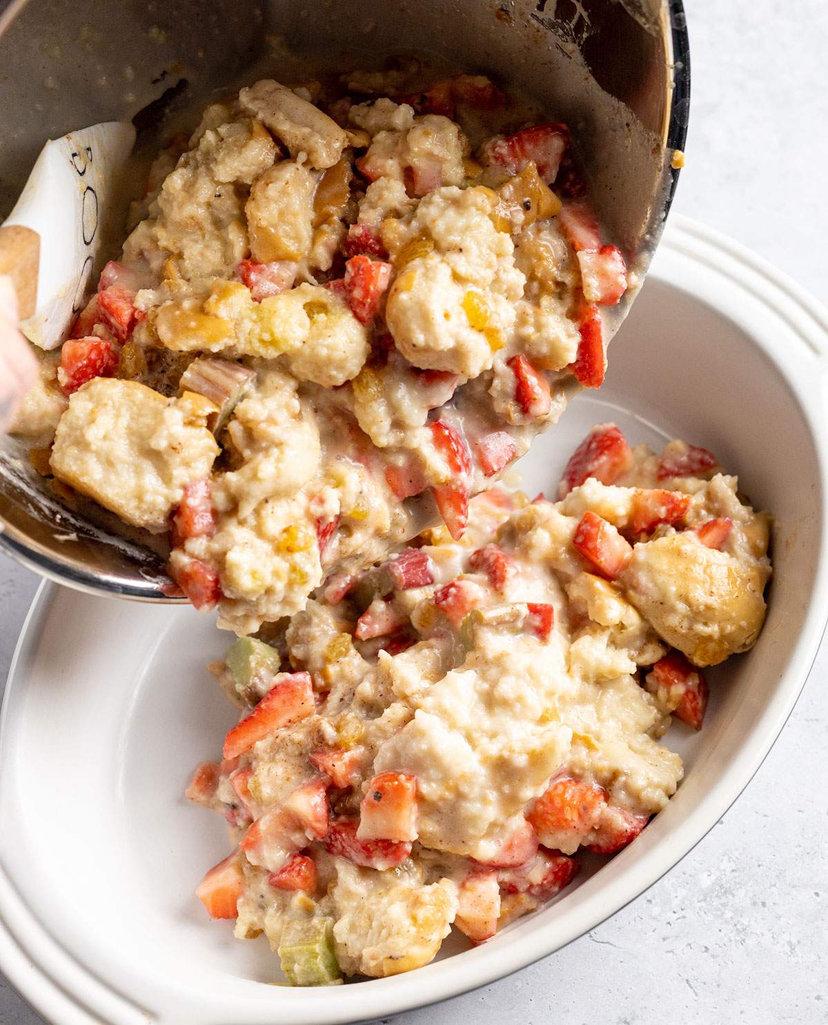 Transferring vegan bread pudding mix with strawberries and rhubarb to an oven dish.