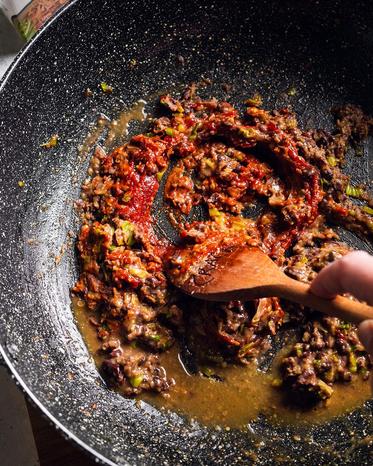 Stirring Gochujang paste into black bean sauce in a large wok.