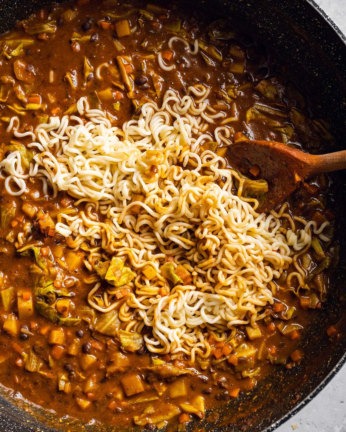 Cooked Ramen noodles added onto Vegan black bean ramen sauce in a large wok.