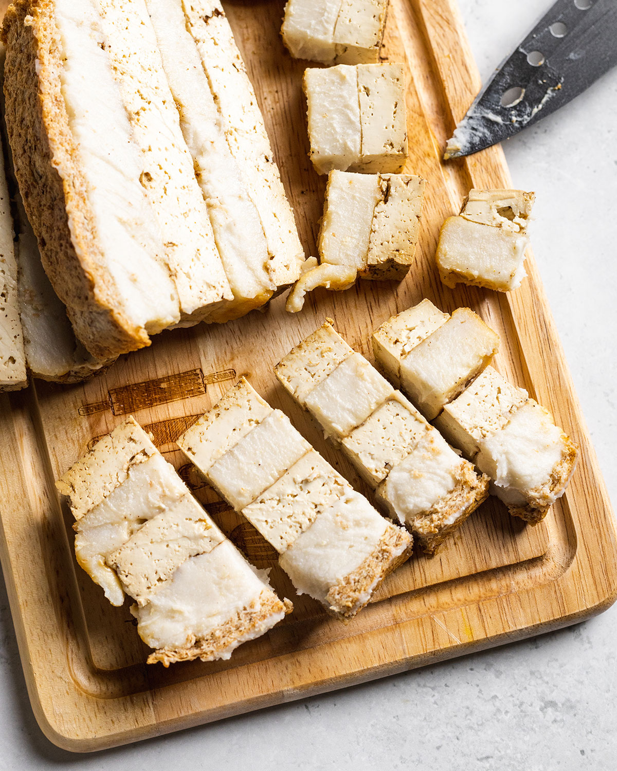 Chopped pieces of vegan pork belly on a wooden board next to a sliced pork belly block.