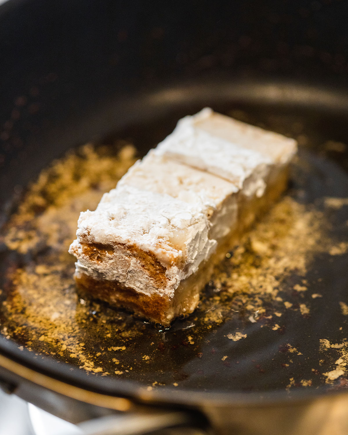 A large piece of vegan pork belly covered in cornstarch frying in hot oil.