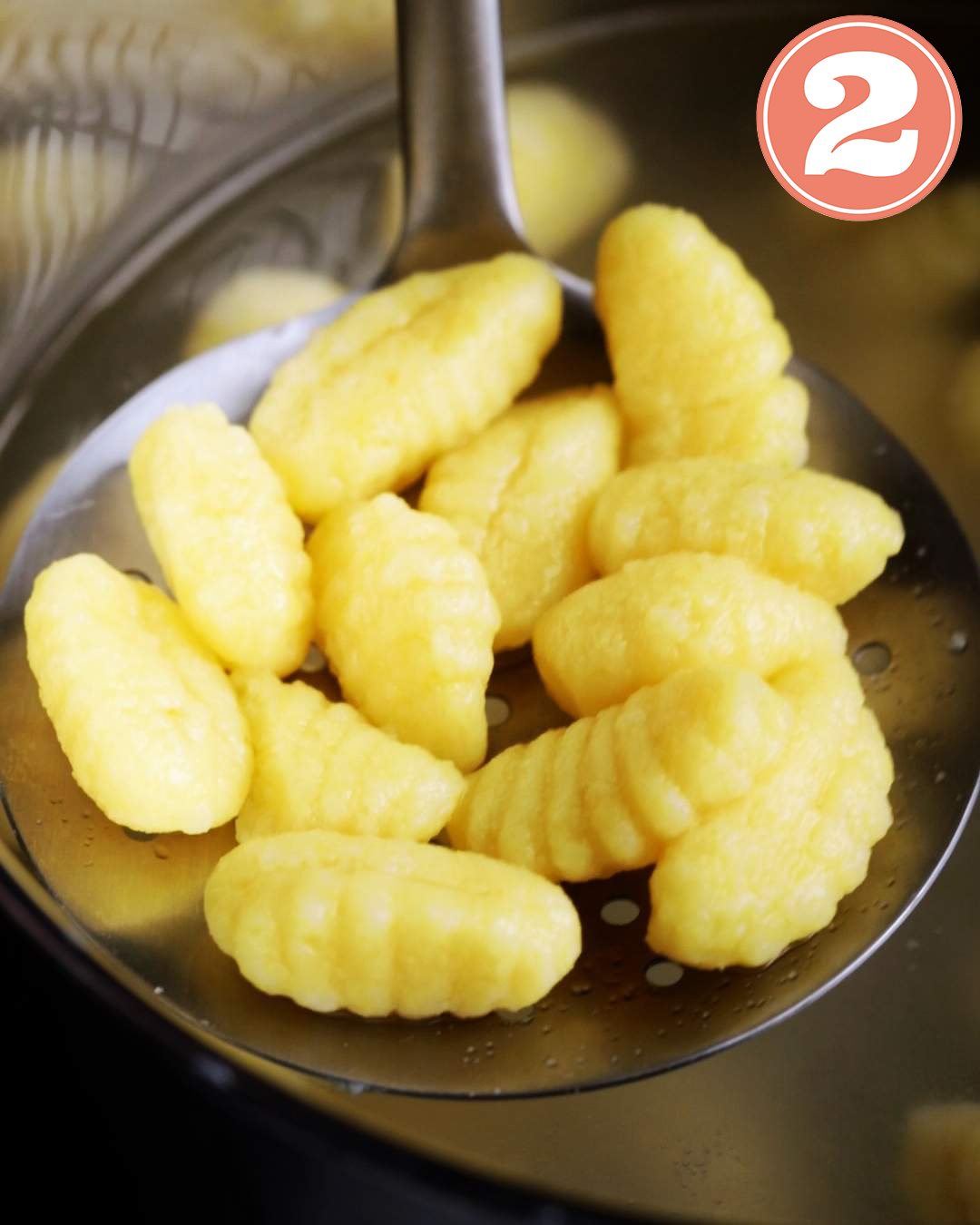 Lifting cooked gnocchi out of hot water with a slatted spoon.