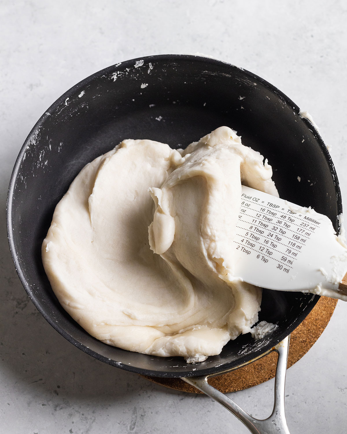 Thickened white paste for vegan pork belly fat in a non-stick pan with a spatula stirring.