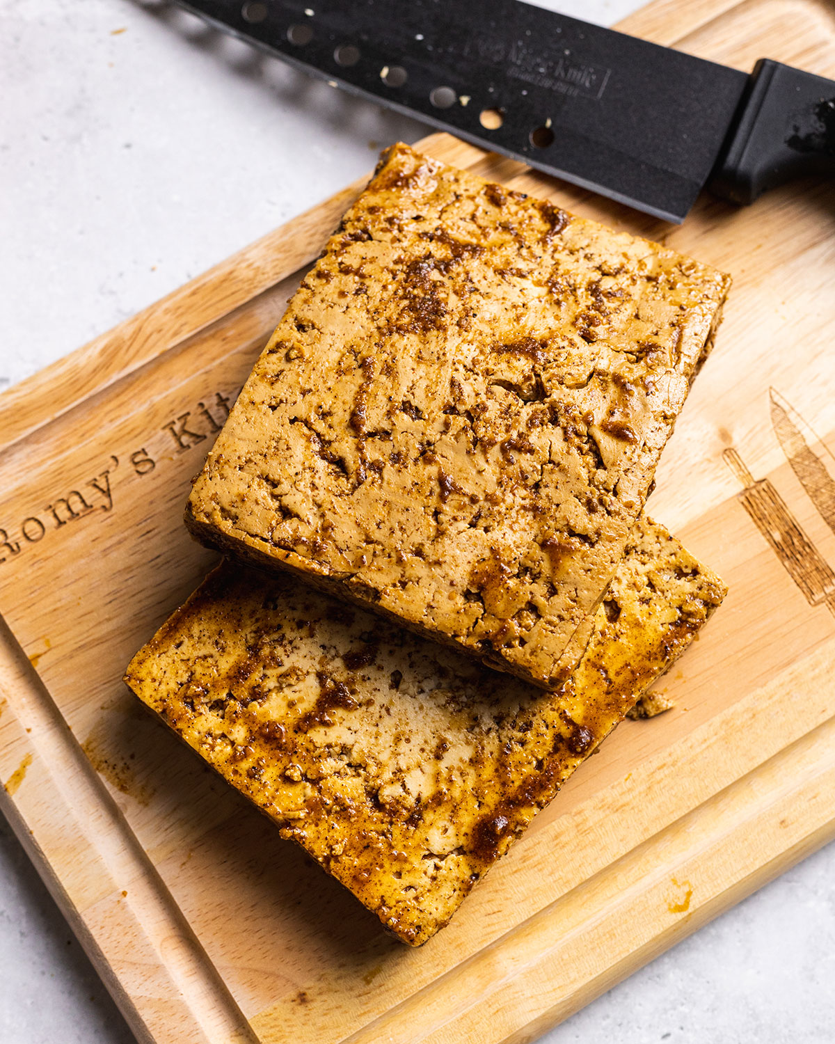 Marinated tofu block sliced into 2 halves on a chopping board.