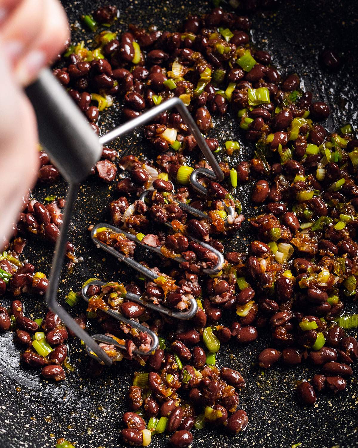 Mashing black beans into sauce in a wok.